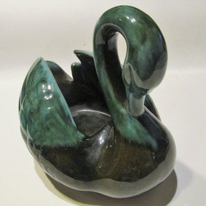 May include: A green glazed ceramic swan planter. The swan has a long neck and is in a sitting position. The planter is designed to hold small plants or flowers.