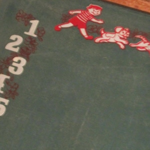 May include: Vintage chalkboard with white numbers 1 through 5 and red illustrations of a boy, dog, and cat. The chalkboard has a green surface and a wooden frame. The illustrations appear to be in motion.