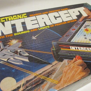 May include: A vintage board game box featuring a fighter jet in flight with a blue and black background. The game is called "Electronic Intercept" and is described as a "search and destroy game" with the "sounds and lights of fighter attack".