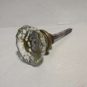 May include: A clear glass door knob with a brass base and a metal spindle.