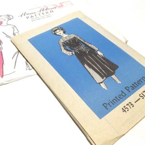 May include: Vintage sewing pattern for a dress, featuring a woman wearing a black dress with a white lace collar and long sleeves. The pattern is labeled "Printed Pattern 4573 - SIZE 12".