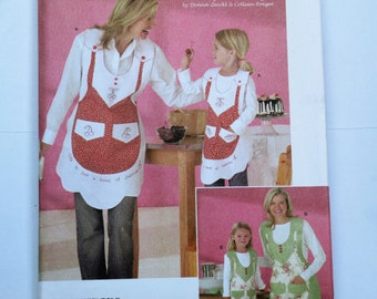 May include: Two pairs of matching aprons, one red with white trim and the other green with white trim. The aprons have a pocket and a cherry design. The text on the red apron says "Life is just a bowl of cherries".