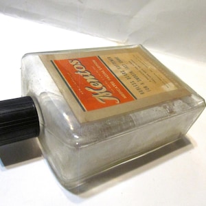 May include: Vintage glass bottle of Kentos medicated facial lotion. The bottle has a black cap and a label with the Kentos logo in red and white. The label also includes text about the product's use for a smooth, fast shave.