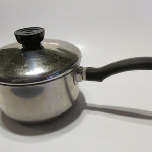 May include: A silver saucepan with a black handle and a lid with a black knob. The saucepan is on a white surface.