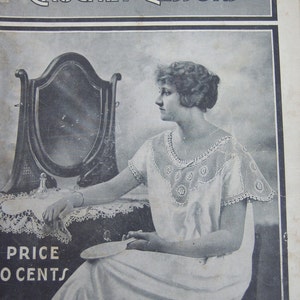 May include: A vintage instructional booklet titled Royal Society Crochet Lessons Vol 1 No 8. The cover features a black and white photograph of a person wearing a light-colored garment with a decorative crocheted collar, sitting before a mirror.