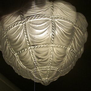 May include: A white glass lampshade with a geometric design of rope and fabric drapes. The lampshade is frosted and has a delicate, intricate pattern.