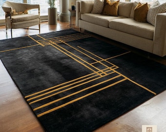 Op de afbeelding: Een groot, rechthoekig zwart tapijt met een geometrisch goudkleurig ontwerp. Het tapijt ligt op een houten vloer in een woonkamer, met een bank, stoel en raam op de achtergrond. Het ontwerp van het tapijt heeft rechte lijnen en rechthoekige vormen.
