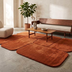 May include: A large area rug composed of multiple interconnected, rounded rectangular segments in a solid, deep burnt orange color. The rug features a soft, plush texture and covers a significant portion of the floor space in the room.