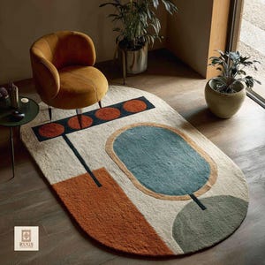 Könnte beinhalten: Ovaler Teppich mit abstraktem Design. Der Teppich hat einen beigen Hintergrund mit geometrischen Formen in Orange, Türkis und Grün. Ein senffarbener Stuhl befindet sich über dem Teppich. Das Wort "RUGS" ist in der Ecke zu sehen.