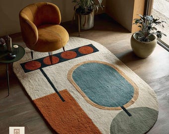 May include: An oval-shaped area rug with an abstract design. The rug features a beige background with geometric shapes in orange, teal, and green. A mustard-colored chair sits above the rug. The rug has the word "RUGS" in the corner.