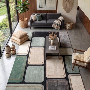 Peut inclure: Un grand tapis rectangulaire présentant un motif géométrique composé de blocs aux coins arrondis dans des tons vert sauge, crème, gris anthracite et noir. Le design inclut de fines lignes de bordure contrastées autour de chaque bloc.