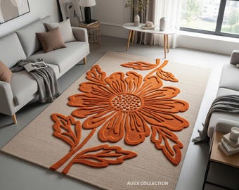 May include: A beige rectangular rug with a large orange floral design. The flower has a detailed center and petals, with matching orange leaves and stems. The rug is in a living room setting with sofas and a coffee table.