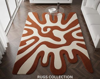 May include: A large, abstract area rug with a brown and cream pattern. The rug has a unique, flowing design with rounded shapes. The text "RUGS COLLECTION" is displayed at the bottom of the rug.
