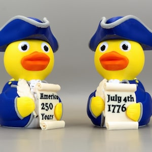 May include: Two yellow rubber duck figurines dressed as Revolutionary War figures. They wear blue coats and hats, and hold scrolls. One scroll reads "America 250 Years," the other "July 4th 1776."