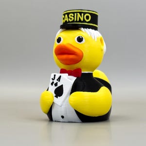 May include: A yellow rubber ducky wearing a black and white tuxedo, a red bow tie, and a black hat with "CASINO" printed on it. The duck holds a card with the Ace of Spades. A fun, novelty item.