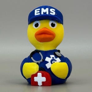 May include: A yellow rubber duck wearing a blue EMS uniform and cap with the word "EMS". The duck has an orange beak, a stethoscope, and a red first aid kit with a white cross.
