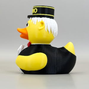 May include: A yellow rubber duck wearing a black tuxedo, a red bow tie, and a black hat with the word "NO" on it. The duck has white hair and an orange beak. A fun novelty item.