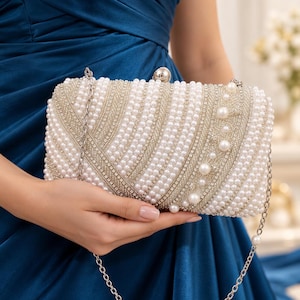 May include: A rectangular clutch bag featuring alternating diagonal stripes of white pearls and silver-toned rhinestones. The bag includes a silver-toned metal frame, a round clasp closure, and a detachable silver-toned metal chain shoulder strap.