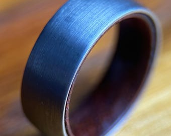 May include: A brushed silver ring with a dark brown wood inlay. The ring is a simple design with a smooth finish.