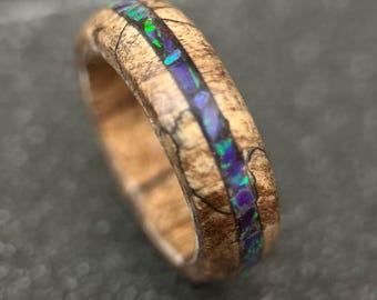 May include: A wooden ring with a thin inlay of iridescent opal. The ring is brown with a natural wood grain pattern.