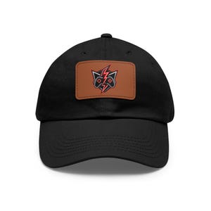 Könnte beinhalten: Schwarze Baseballkappe mit einem braunen rechteckigen Aufnäher mit einem rot-schwarzen Gaming-Controller-Design mit einem Blitz. Die Kappe hat einen gebogenen Schirm und eine strukturierte Krone.