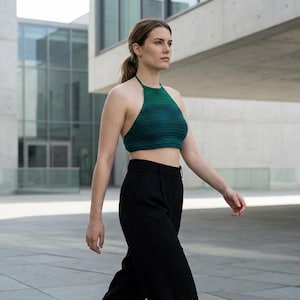 May include: A green and blue halter top. The top is a cropped style and is paired with black pants. The image is taken outdoors, with a modern building in the background.