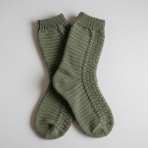 Puede incluir: Un par de calcetines de punto verde oliva, con un patrón texturizado en la parte delantera y puños acanalados. Los calcetines están hechos de un material suave y cálido, ideal para el frío. Los calcetines miden unos 30 cm de largo.