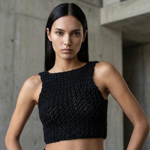 May include: A black, sleeveless crop top with a textured, woven design. The top has a square neckline and is made of a dark material. The model is wearing the top and has long, dark hair.