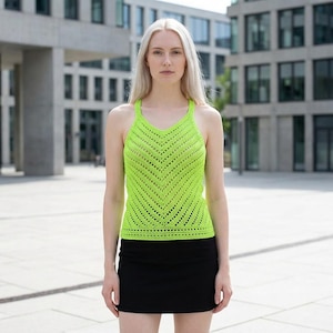 May include: A neon green, open-weave halter top with a chevron pattern is paired with a black mini skirt. The top has a V-neck and a fitted silhouette. The outfit is worn outdoors in front of a modern building.