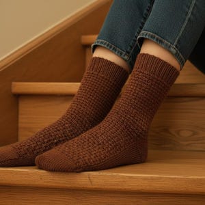 May include: A pair of mid-calf length socks in a solid brown color, featuring a textured waffle-knit pattern on the leg and foot, with a ribbed cuff at the top and a smooth knit finish at the toe area, crafted from a soft yarn material.