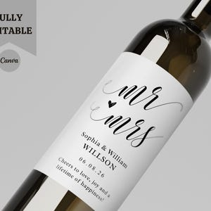 May include: A clear wine bottle with a white label. The label has the words "mr mrs" in cursive script, a heart symbol, and the names Sophia & William WILLSON with the date 06.08.26. The text "Cheers to love, joy and a lifetime of happiness!" is also present.