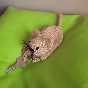 K&ouml;nnte beinhalten: Ein geh&auml;kelter Katzen-Schl&uuml;sselanh&auml;nger in Braun und Wei&szlig;. Die Katze h&auml;lt einen silbernen Schl&uuml;ssel im Maul.