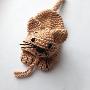 K&ouml;nnte beinhalten: Ein geh&auml;keltes braunes Katzenspielzeug mit schwarzen Augen und Schnurrhaaren. Die Katze liegt auf dem Bauch mit eingerolltem Schwanz.