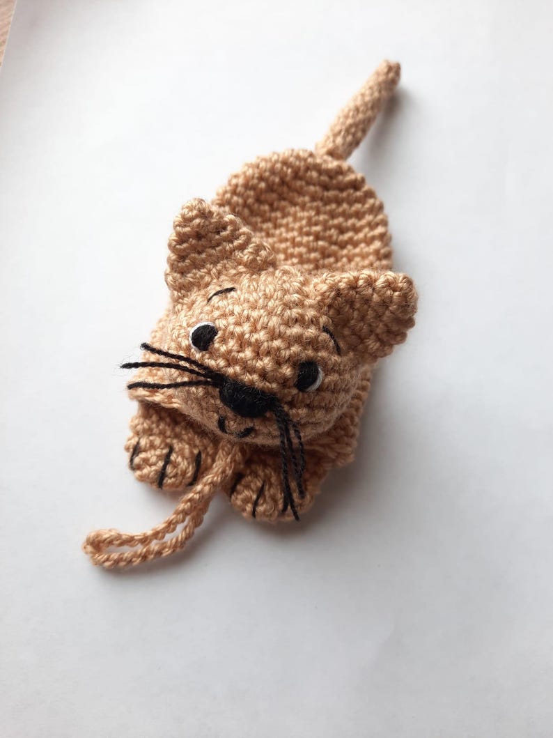 K&ouml;nnte beinhalten: Ein geh&auml;keltes braunes Katzenspielzeug mit schwarzen Augen und Schnurrhaaren. Die Katze liegt auf dem Bauch mit eingerolltem Schwanz.
