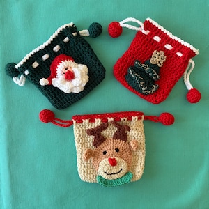 May include: Three handmade crochet Christmas gift bags. One is dark green with a Santa Claus design, one is red with a Christmas tree, and the third is beige with a reindeer. Each bag has a drawstring closure and a pom-pom.