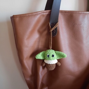 May include: A brown leather tote bag with a green crocheted Yoda keychain attached to the handle.