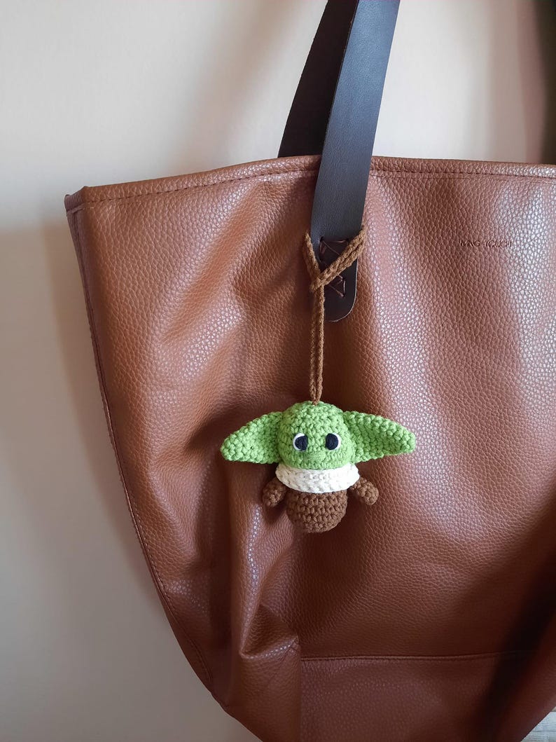 May include: A brown leather tote bag with a green crocheted Yoda keychain attached to the handle.
