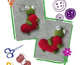 May include: A crochet pattern for a frog key chain holding a red heart. The frog is green with white eyes and a silver key ring. The text "Frogy Key Chain Pattern" is at the top. Other craft supplies are also shown.