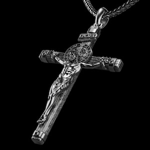 May include: A silver-toned crucifix pendant with a detailed depiction of Jesus Christ on the cross. The pendant hangs from a matching chain. The cross features the letters INRI at the top and a circular emblem behind the figure.
