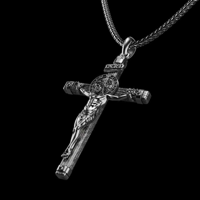 May include: A silver-toned crucifix pendant with a detailed depiction of Jesus Christ on the cross. The pendant hangs from a matching chain. The cross features the letters INRI at the top and a circular emblem behind the figure.
