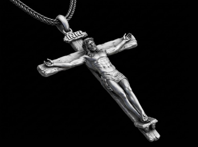 May include: A silver-colored pendant necklace featuring a detailed depiction of Jesus on a cross. The cross has a rustic, wooden appearance, and the figure is intricately sculpted. The necklace chain is a woven design, and the background is black.