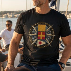 May include: A black short-sleeved t-shirt featuring a large circular graphic on the chest. The design includes a compass rose background with three stacked nautical signal flags in yellow, red with a yellow cross, and white with a red circle.
