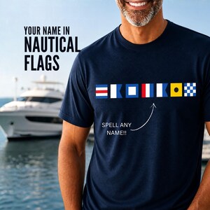 May include: Navy blue t-shirt with nautical flag designs spelling out a name. The shirt features the text "YOUR NAME IN NAUTICAL FLAGS" and "SPELL ANY NAME!!" A white yacht is visible in the background.