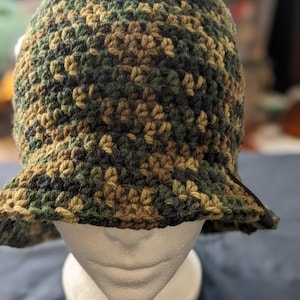 May include: A crocheted bucket hat in a camouflage pattern with green, brown, and black yarn.