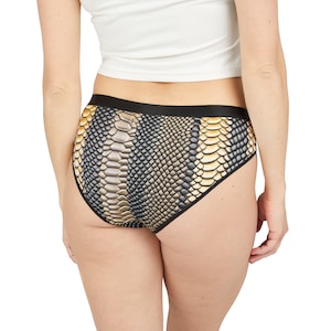 以下が含まれることがあります： 黒と金のヘビ柄のショーツで、黒いウエストバンドが付いています。