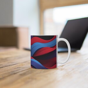 Könnte beinhalten: Weiße Keramik-Kaffeetasse mit einem lebendigen abstrakten Design aus fließenden roten, blauen und violetten Wellen. Die Tasse hat einen Standardgriff und steht auf einer Holzoberfläche, mit einem Laptop im Hintergrund.
