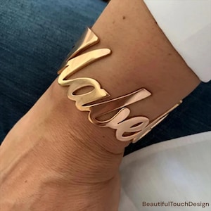 Pode incluir: Pulseira de metal dourado com o nome "Isabel" escrito em cursivo.