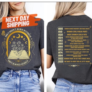 May include: Dark gray heather t-shirt with the text "THEY DIDN'T BURN WITCHES THEY BURNED WOMEN" and a graphic of an open book with flowers. The back of the shirt lists women's rights milestones. The shirt is paired with blue jeans.