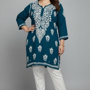 May include: A teal tunic featuring intricate white floral embroidery around the neckline and scattered across the front, with three-quarter length sleeves and a split neckline, paired with solid white straight-leg trousers and beige heels.