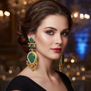 May include: Ornate gold earrings featuring large, green, oval gemstones and red accents. The earrings have a drop design with small gold beads. The woman in the image is wearing a black dress.